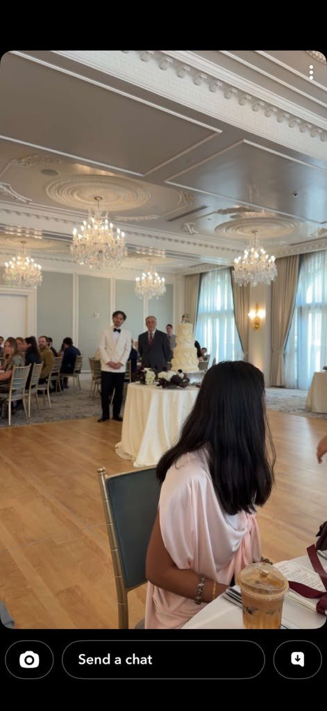 Full view of the Hotel Carmichael chandelier ballroom with guests seated, the wedding cake table, and a server standing by during Laila and Chris's reception